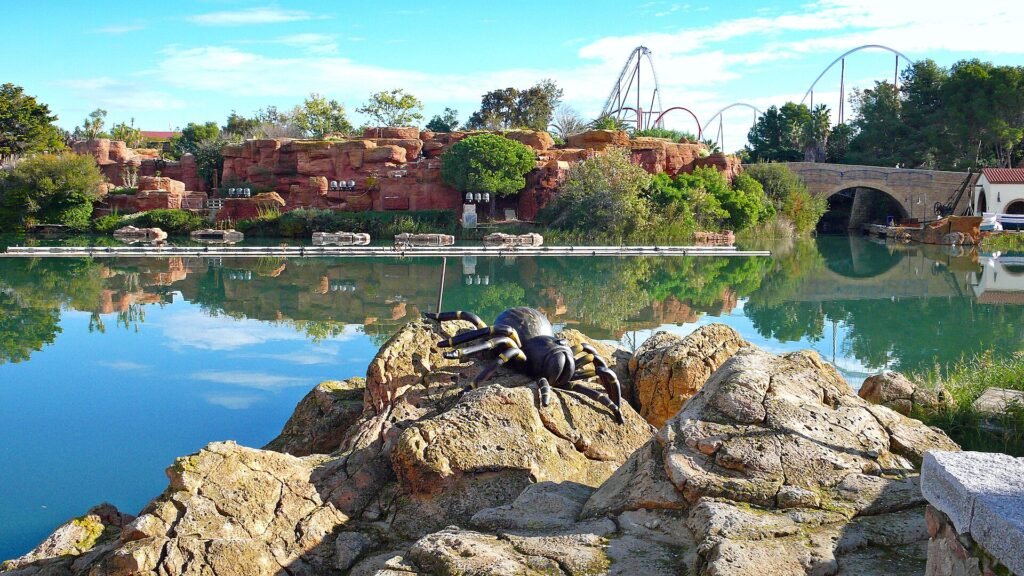 Il lago dell'area Mediterrània a PortAventura Park con rocce, vegetazione e un ragno decorativo di Halloween