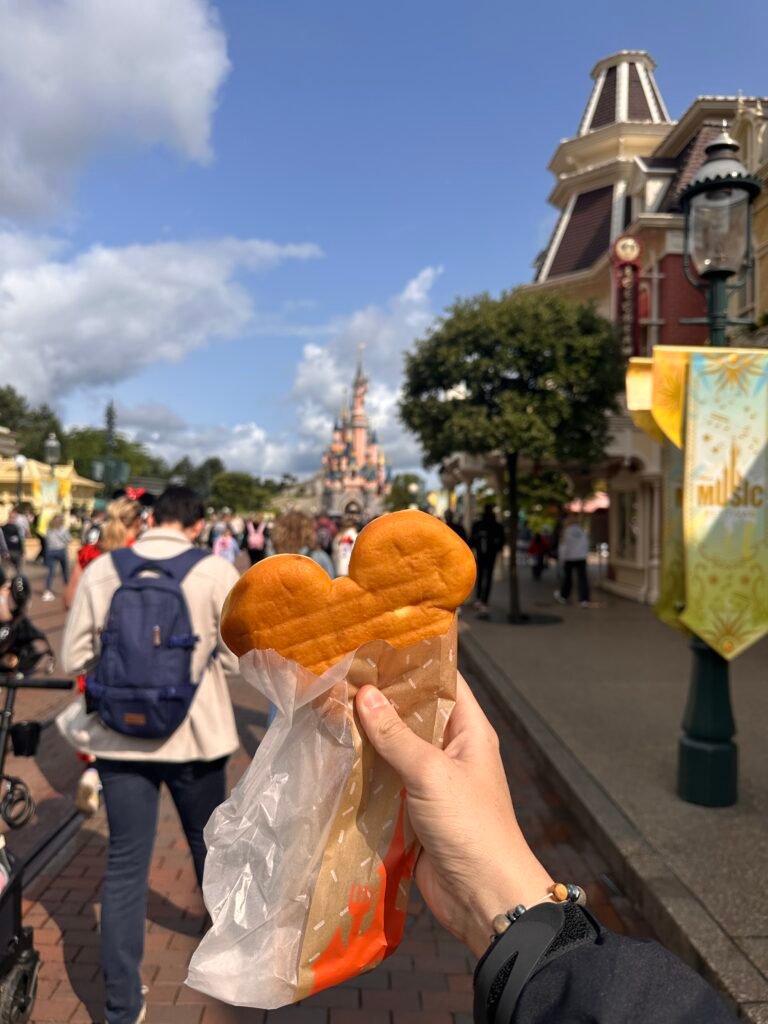 Un beignet a forma di Topolino in un sacchetto di carta, tenuto in mano su Main Street, U.S.A., con il castello sfocato sullo sfondo